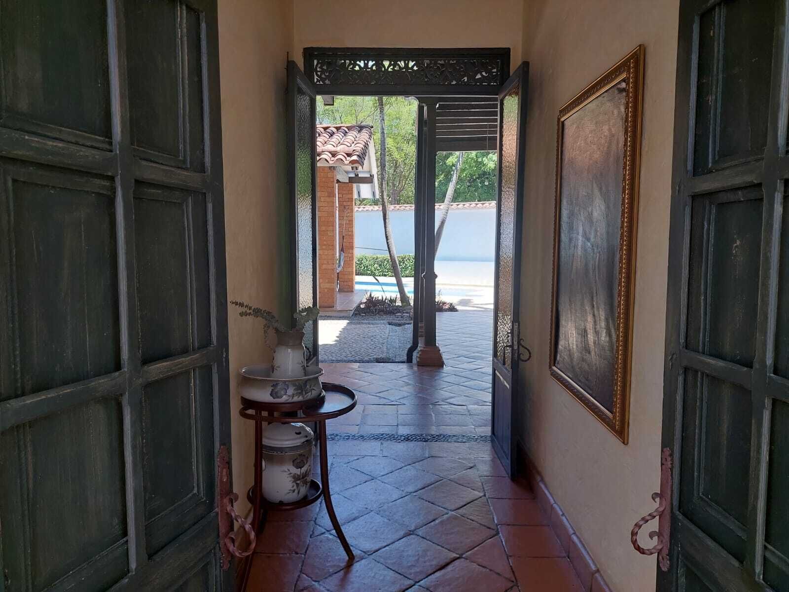 Un couloir carrelé mène à un espace piscine. On y trouve une petite table avec un vase et un tableau encadré accroché au mur.