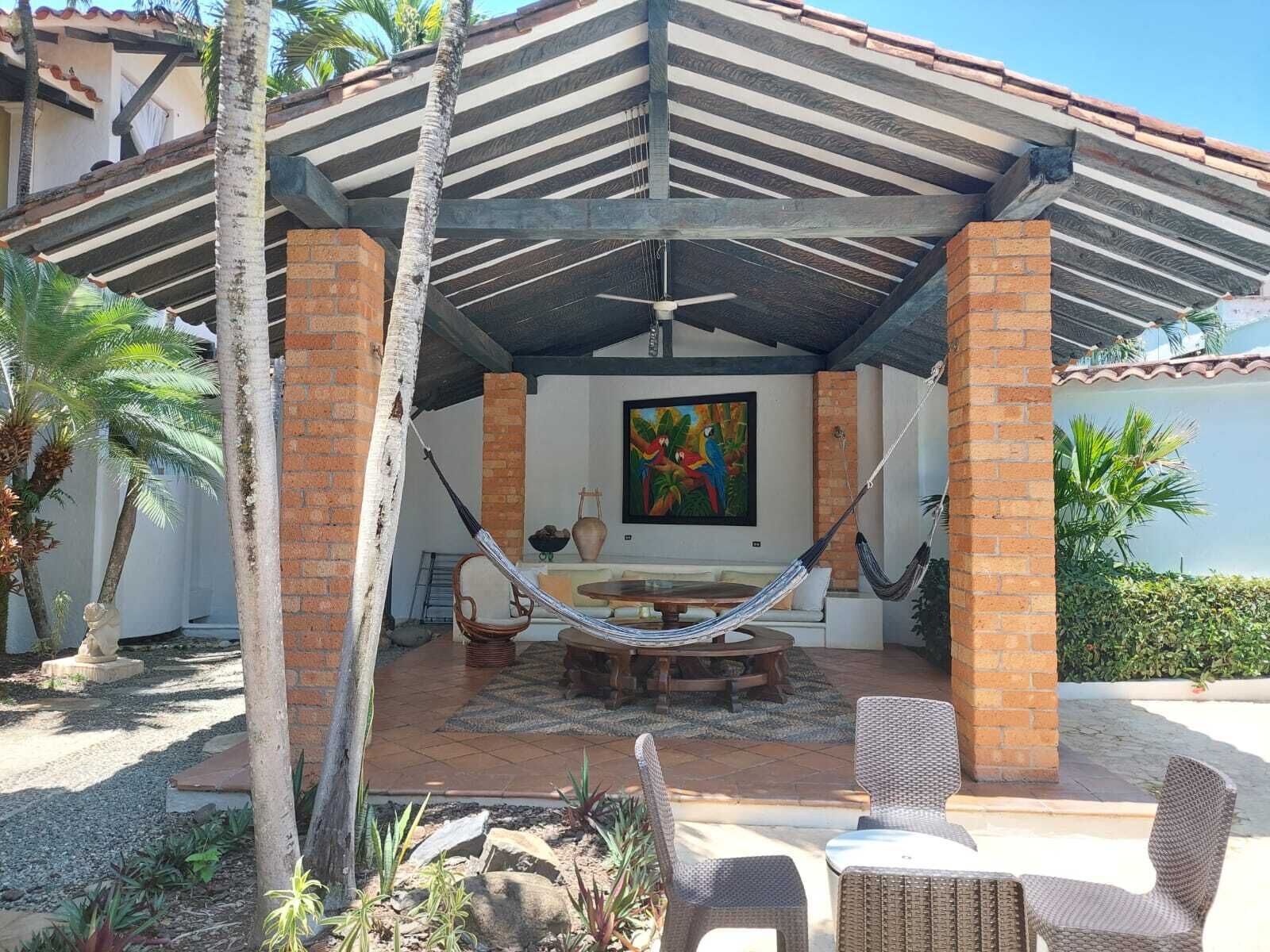 A covered outdoor seating area with a hammock, wicker chairs, and a table.