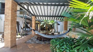 Ein überdachter Patio-Bereich mit einer Hängematte, Gartenmöbeln und Topfpflanzen.