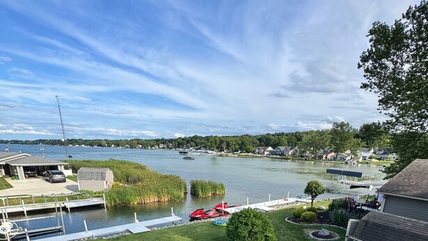 Une terrasse donnant sur un lac, avec un quai, un kayak rouge et un petit abri de jardin.