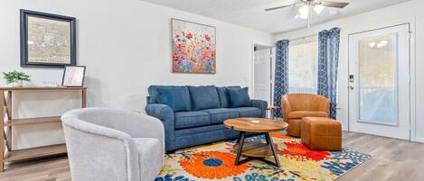 A living room with a blue sofa, a grey armchair, a brown armchair, a small wooden table, and a colorful rug.
