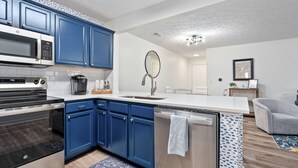 A modern kitchen with blue cabinets, stainless steel appliances, a white countertop, and a small island with a dishwasher.