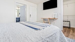 A bedroom with a bed, a desk with a chair, a TV, and a walk-in closet.