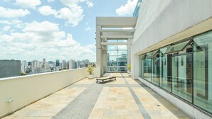 A rooftop terrace with a view of the city skyline, a seating area, and a glass wall. - Queen suite - Berrini (Cidade Monções São Paulo)
