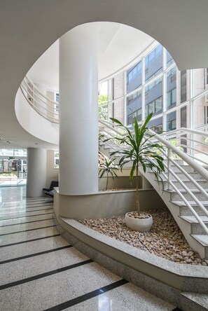 A modern indoor space with a curved staircase, a central column, and a potted palm tree.