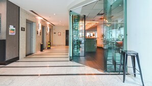 A modern hotel lobby with a glass partition, a reception desk, and a staircase leading to upper floors. - Queen suite - Berrini (Cidade Monções São Paulo)