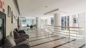 A spacious lobby with a modern design, featuring a long reception desk, comfortable seating area, and large windows offering views of the outside. - Queen suite - Berrini (Cidade Monções São Paulo)