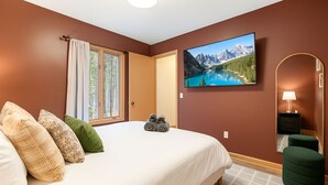 Une chambre à coucher avec un lit, des oreillers, une fenêtre, un tableau, un miroir et une table de chevet.