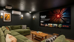 Un salon moderne avec un canapé d’angle, une table basse et un téléviseur fixé au mur diffusant la série « Stranger Things ».