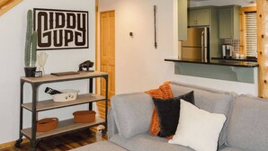 A spacious living area with a grey sofa, wooden staircase, and a kitchen in the background. - Luxury Chalet + Arcade  3BRD Dogs OK (Redmond)