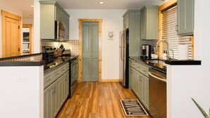 A kitchen with light green cabinets, stainless steel appliances, and a wooden floor. - Luxury Chalet + Arcade  3BRD Dogs OK (Redmond)