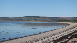 A coastal landscape with a pebble beach and calm water. - Fishers Cottage (Inverness)