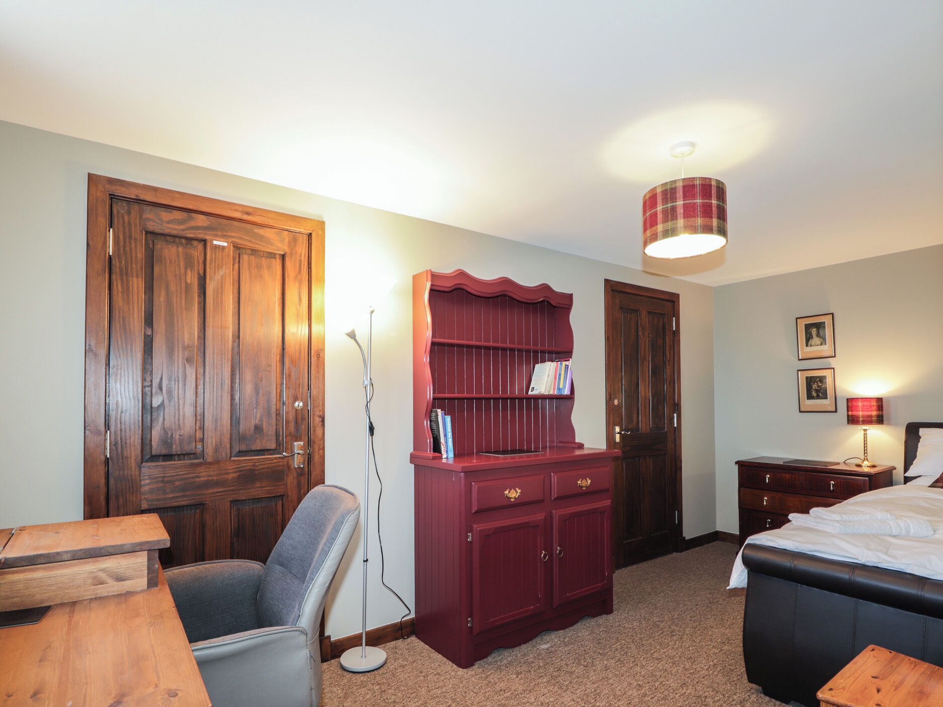 Una habitación con un escritorio de madera, una estantería roja, una cama y una lámpara de pie.