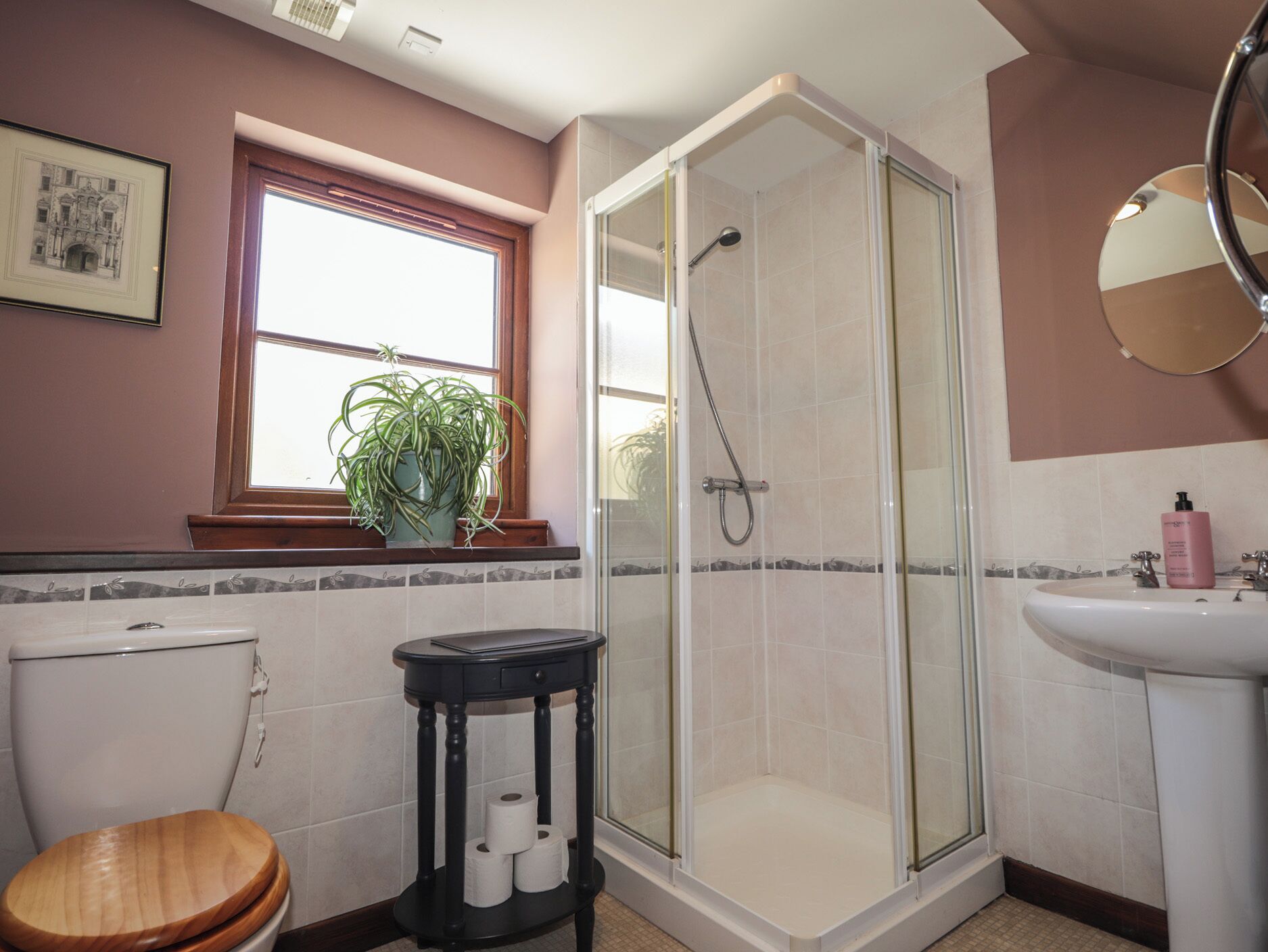 Ein Badezimmer mit Toilette, Waschbecken, Dusche und einem Fenster mit Pflanze.