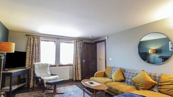 A living room with a sofa, armchair, coffee table, and a TV.