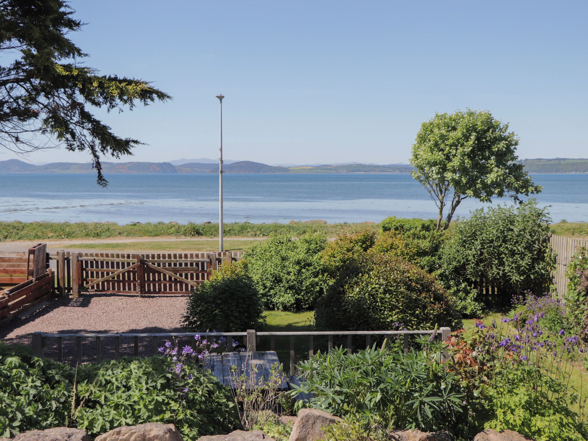 Ein Küstengarten mit Holzzaun, einer Laterne und Blick aufs Meer.
