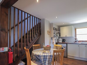 A kitchen with wooden cabinets, a dining table with chairs, a staircase with wooden railings, and a red fire extinguisher.
