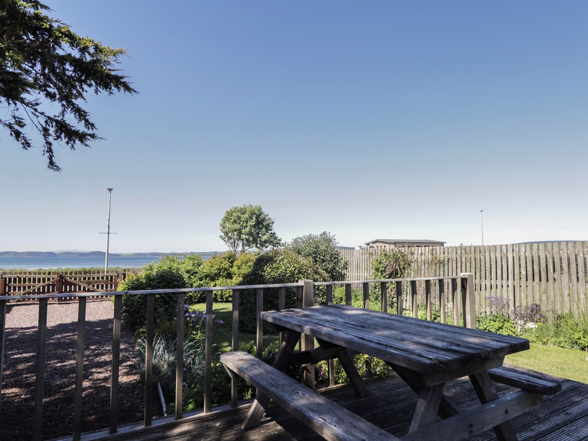 An outdoor wooden deck with a picnic table and a view of the sea and hills.