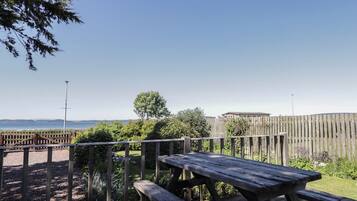 An outdoor wooden deck with a picnic table and a view of the sea and hills.