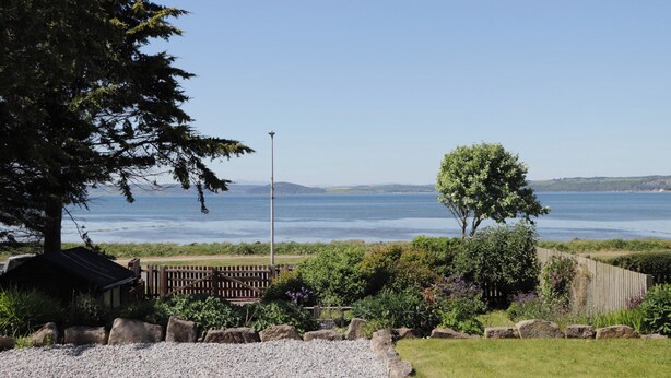 A coastal view with a clear sky, a wooden fence, and a gravel path leading to a small structure. - Fishers Cottage (Inverness)