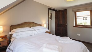 A bedroom with a large bed, a wooden headboard, a bedside lamp, a door, and a window. - Fishers Cottage (Inverness)