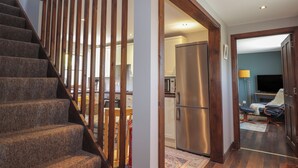 A staircase with wooden railings leading to a kitchen area with a stainless steel refrigerator. - Fishers Cottage (Inverness)