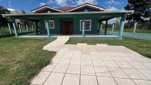 A house with a tiled driveway leading to a front door, surrounded by a green lawn and a low fence.