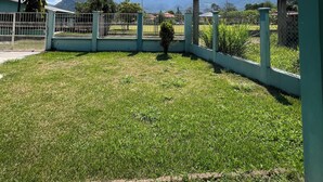 A view from a covered outdoor area with a grassy lawn, a metal fence, and a mountain in the background.