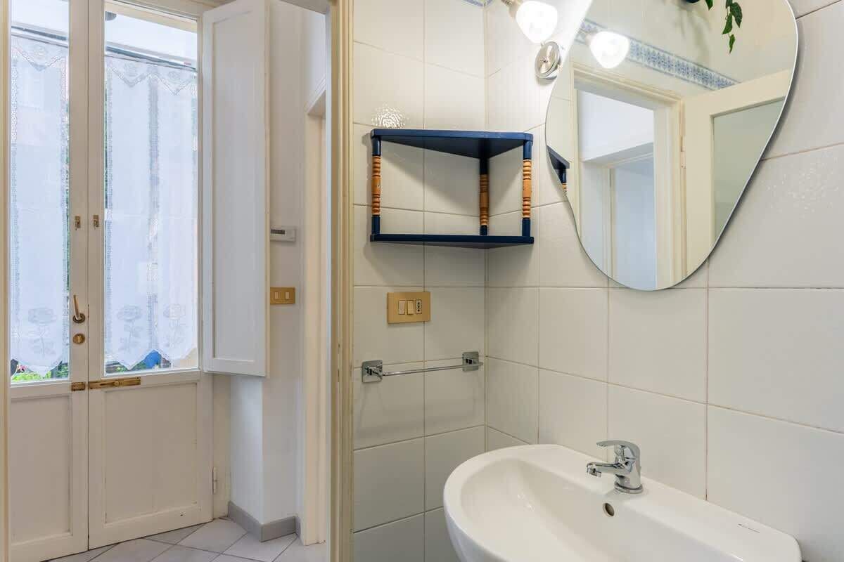 Casa de banho com lavatório branco, espelho e zona de duche.