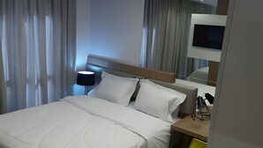 A hotel room with a bed, a desk with a lamp, a chair, and a TV mounted on the wall. - Apto 2 Quartos com Churrasqueira no Sky Batel · Piscina Aquecida e Sauna (Curitiba)