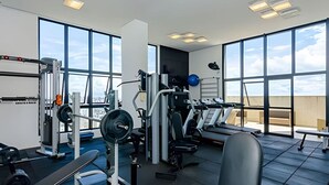 A gym with various exercise equipment, large windows, and a view of the sky. - Apto 2 Quartos com Churrasqueira no Sky Batel · Piscina Aquecida e Sauna (Curitiba)