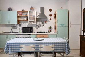 A compact kitchen with a microwave, stove, and cabinets, a dining table with chairs, and a refrigerator.