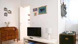 Ett rum med en byrå i trä, en tv på ett vitt stativ, en lampa och en gammal resväska.