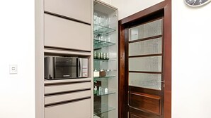 A kitchen with a microwave, open cabinets, and a glass-fronted cabinet with shelves. - Apartamento 3 Quartos 116m² no Batel Curitiba (Curitiba)