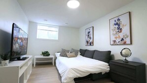 Een moderne slaapkamer met een bed, nachtkastje, televisie en kunstwerk.