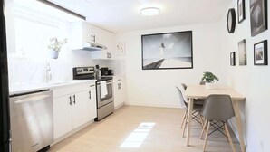 Een moderne keuken met witte kasten, een roestvrijstalen koelkast en een eethoek met een tafel en stoelen.