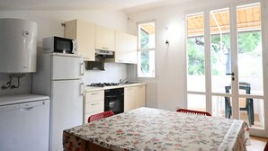 A compact kitchen with a refrigerator, microwave, stove, and oven. There is a dining table with a floral tablecloth and a chair. - M437 – Marcelli, two-room apartment with air conditioning (Marcelli)