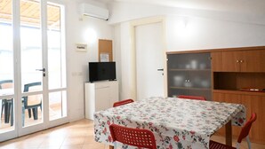 A room with a table, chairs, a television, a cabinet, and a door. - M437 – Marcelli, two-room apartment with air conditioning (Marcelli)