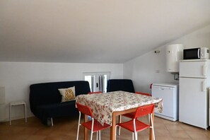 Un espace de vie compact comprenant une table à manger, des chaises rouges, un canapé noir, un réfrigérateur blanc et un four à micro-ondes.