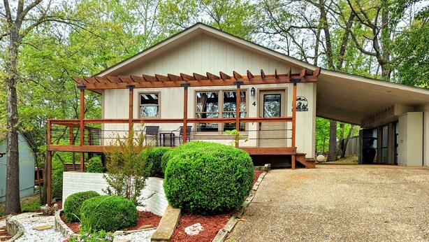 A two-story building with a covered porch, a garage, and a well-maintained garden with flower beds and a gravel driveway. - Your Adventure Basecamp in NWA (Bella Vista)