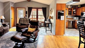 A living room with a leather chair, a wooden dining table, and a kitchen area with wooden cabinets and appliances. - Your Adventure Basecamp in NWA (Bella Vista)