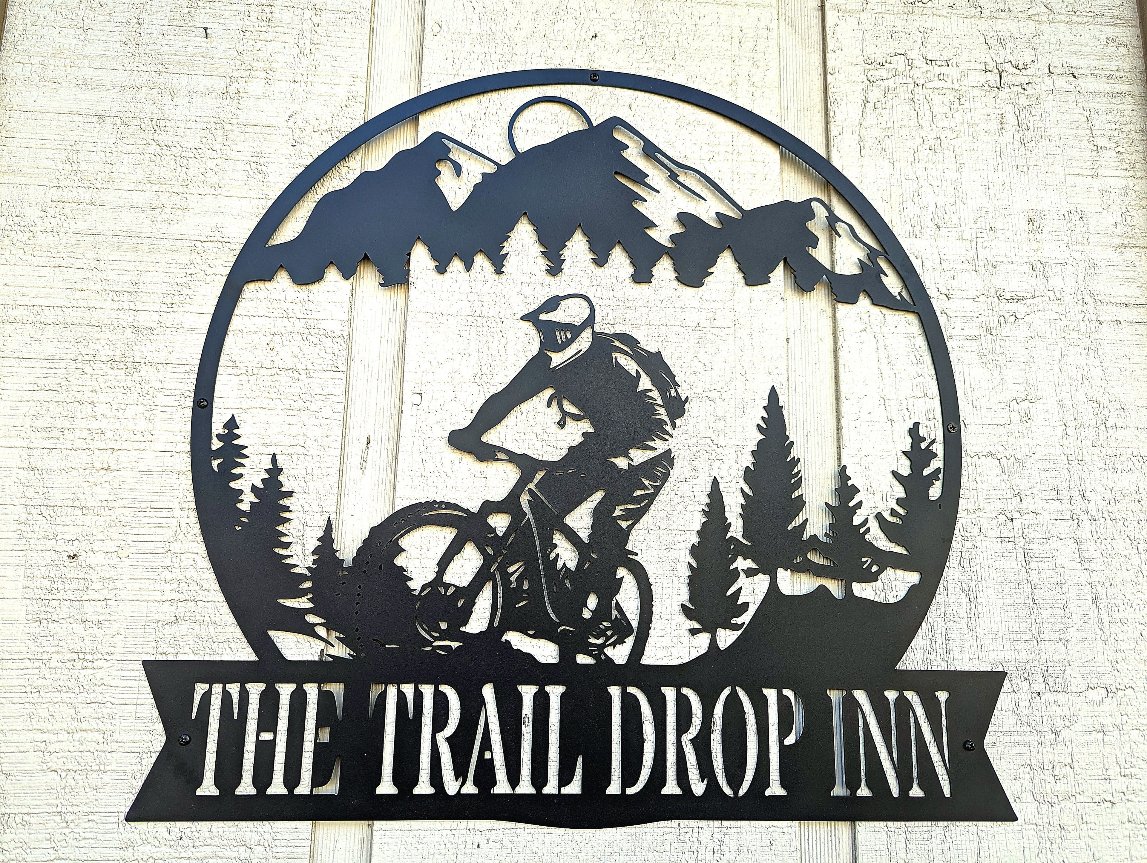 Un logo raffigurante un ciclista e montagne, con il testo 'THE TRAIL DROP INN'.