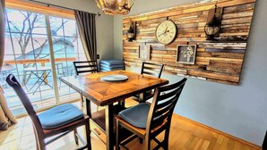 A dining area with a wooden table and chairs, a chandelier, and a wall-mounted clock. - Your Adventure Basecamp in NWA (Bella Vista)