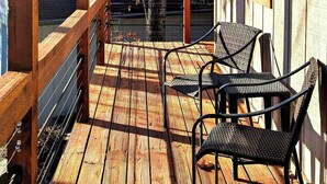 A wooden deck with two wicker chairs and a small table, overlooking a backyard with a tree and a house in the background. - Your Adventure Basecamp in NWA (Bella Vista)