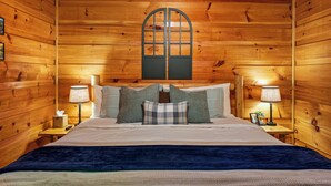 Ein schlicht eingerichtetes Schlafzimmer im Chalet-Stil mit einem großen Bett, zwei Nachttischlampen und einem Fenster mit dekorativem Bogen.
