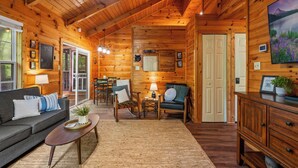 A cozy log cabin interior with a sofa, armchairs, a dining table, and a fireplace.