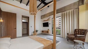 A bedroom with a four-poster bed, a wooden ceiling, a television, a brown leather armchair, and a small round table. - Poblado, 5 min to San Lucas Plaza, Free parking (Medellín)