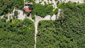 Luchtbeeld van een strand met een kleine groep gebouwen, omringd door weelderige begroeiing.
