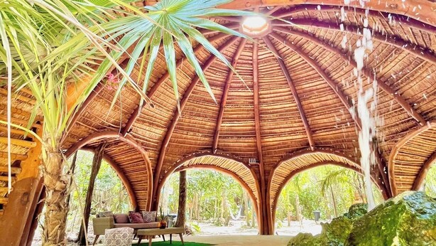 Een paviljoen met rieten dak, een centraal zitgedeelte en een natuurlijke omgeving.