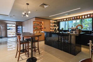 A modern bar area with a polished floor, wooden bar stools, a counter with a coffee machine, and shelves with bottles.